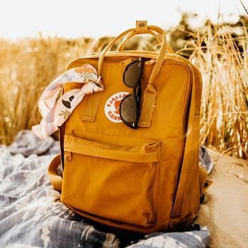 Fjallraven Kanken on the beach with sunglasses and scarf tied around it