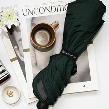 Umbrella done up, next to a coffee cup and on top of magazines