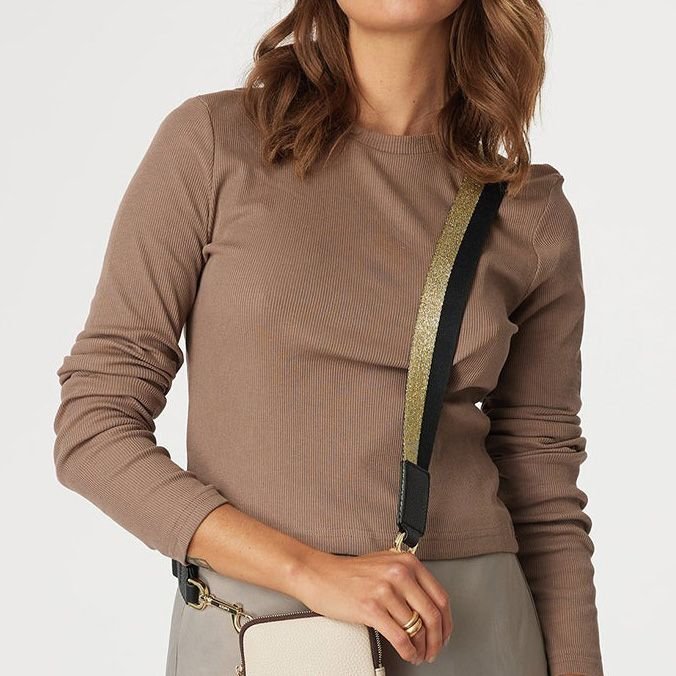 Woman wearing a crossover bag featuring a The Saben Feature Strap in gold and black.