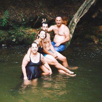Family sitting on a fallen tree trunk at Kerosene Creek in Rotorua