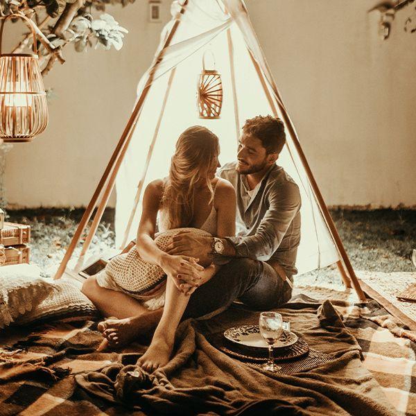 A couple in a little tent looking at eachother after dinner and wine