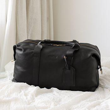Black leather duffle bag on a white bed