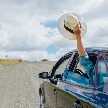 Person riding in a car with the windows down and holding their sun hat out the window