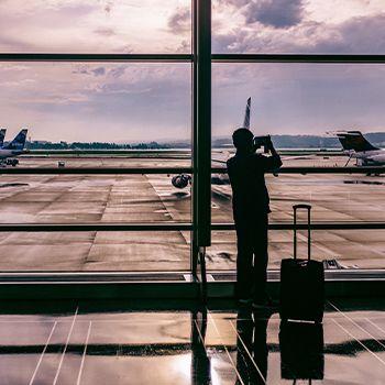 silhouetted man at airport window with his luggage, taking pics of planes