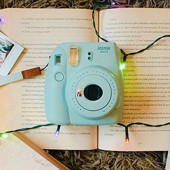 Blue Instax mini 9 polaroid camera on top of a book with fairy lights